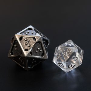 Hollow metal braille d20 next to a standard sized clear acrylic d20 for comparison. The braille d20 is about twice the size.