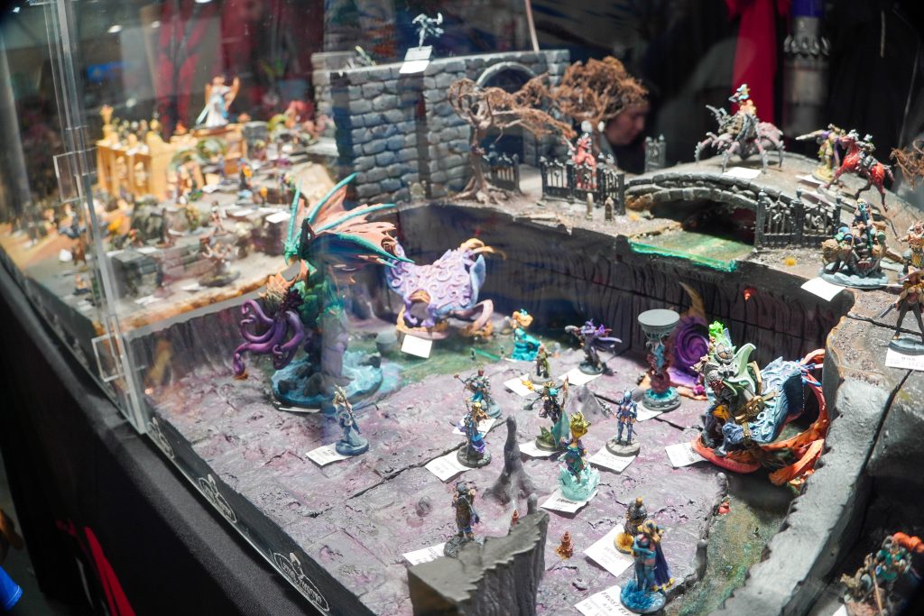 A sprawling diorama of a fantasy battlefield featuring multiple painted miniatures in various poses, displayed at the Lethal Shadows booth.