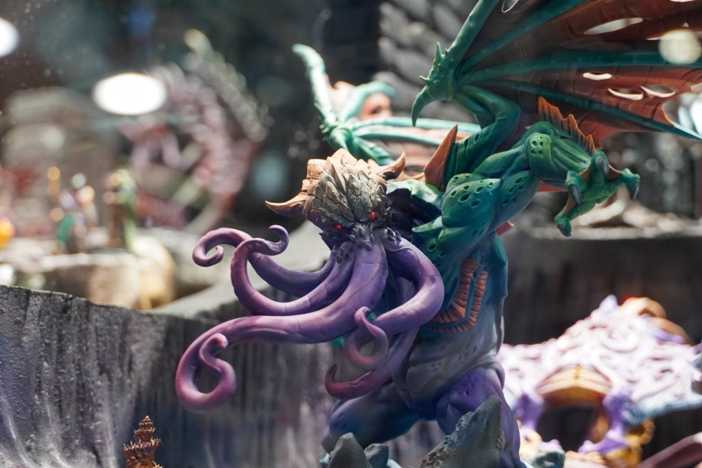 A close-up of a strikingly painted miniature featuring a tentacled, dragon-like creature with vivid purple and green hues, displayed at the Lethal Shadows booth.