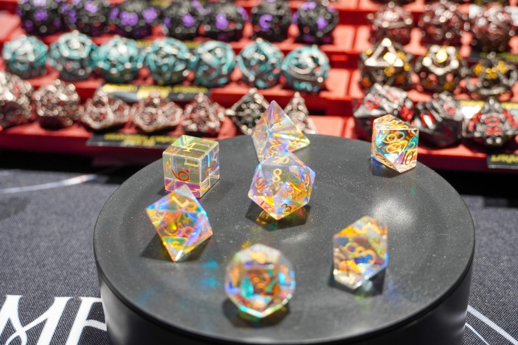 Holographic, iridescent dice set on a rotating display at the Lethal Shadows booth, surrounded by other intricate dice designs.