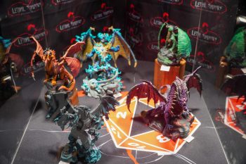A showcase of large, painted dragon miniatures and other fantastical creatures arranged on a D20-themed mat at the Lethal Shadows booth.