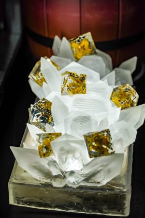 Close-up of a decorative dice display featuring translucent white resin spikes holding gold-accented dice with glitter inside, set against a wooden barrel backdrop.